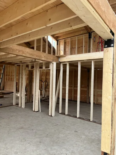 Close interior construction view of framed partition walls beneath exposed timber beams and roof structure