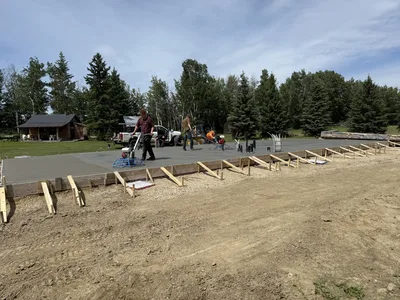 Wide view of a crew finishing a newly poured concrete slab foundation with formwork around the perimeter